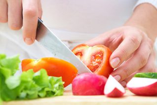 Person skär grönsaker med kniv i köket.